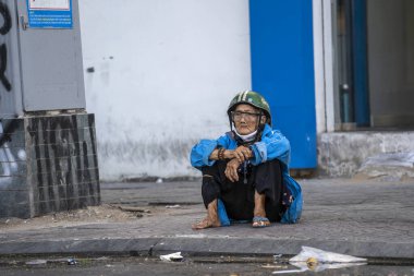 Ho Chi Minh, Vietnam - 21 Mart 2020: Motosiklet kasklı zavallı Vietnamlı yaşlı kadın Ho Chi Minh, Vietnam şehir merkezinde bir kaldırımda oturuyor.