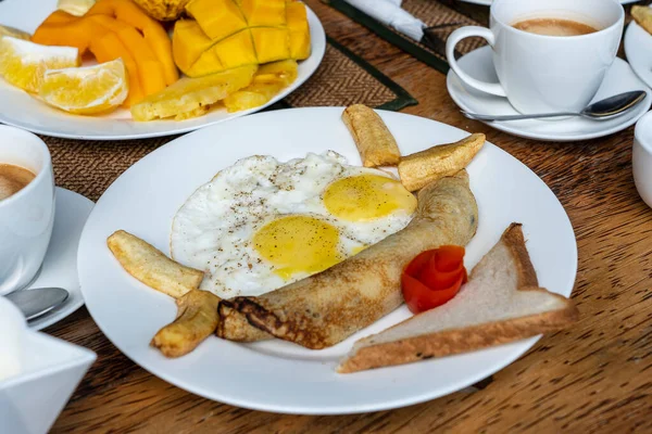 在非洲坦桑尼亚桑给巴尔岛的酒店餐厅附近的海滩上 两个人享用热带早餐 包括水果 炒鸡蛋和香蕉煎饼 顶部视图 表设置 — 图库照片