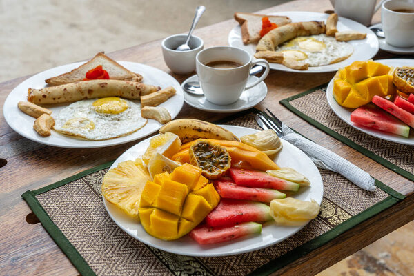 Tropical breakfast of fruit, coffee and scrambled eggs and banana pancake for two on the beach near sea in hotel restaurant, island Zanzibar, Tanzania, Africa, close up. Top view, table setting.