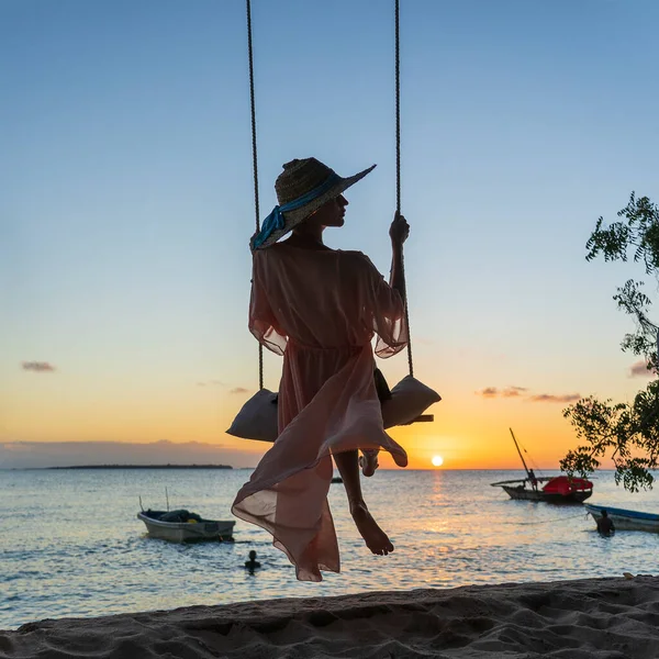 在坦桑尼亚桑给巴尔岛的日落时分 戴着草帽 身穿长袍的美女在海滩上荡秋千 旅行和休假概念 — 图库照片