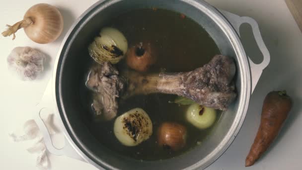 Beef bone in broth in a saucepan with vegetables, top view — Stock Video