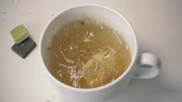 The egg falls into a white cup with clear soup. Slow motion — Stock Video