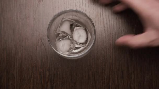 Av is sätta kuber i ett glas whiskey på bordet. ovanifrån — Stockvideo