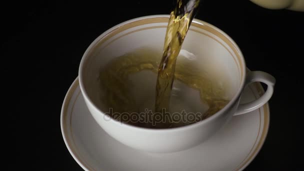 Медленно. Чай наливают в чашку и блюдце на черном фоне — стоковое видео