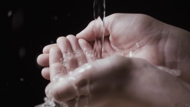 Ροή του νερού σε παιδικά χέρια σε μαύρο φόντο. Αργή mo — Αρχείο Βίντεο