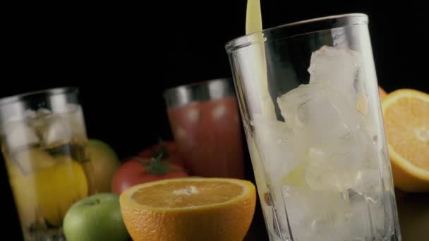 Orangensaft fließt in ein Glas mit Eis auf schwarzem Hintergrund. Zeitlupe. — Stockvideo