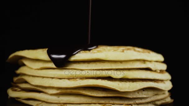 Schokolade wird auf einen Pfannkuchen vor schwarzem Hintergrund gegossen. Zeitlupe — Stockvideo