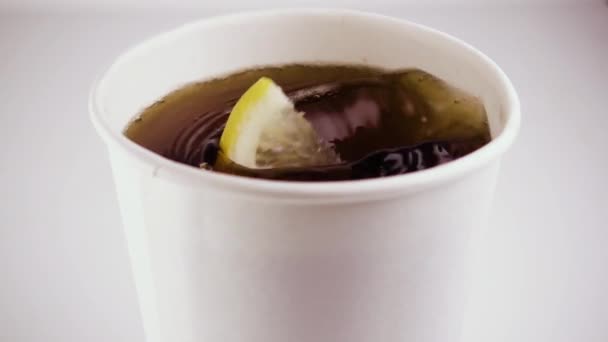 Slow motion. In a cardboard glass with tea falls a lemon — Stock Video