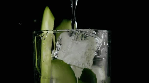 Wasser wird in ein Glas mit Gurke und Eis gegossen. Zeitlupe — Stockvideo