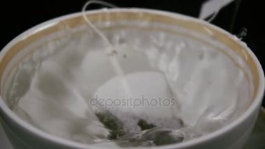 Kaynar su bir fincan çay bir torba atmak. Ağır çekim
