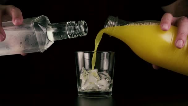 Gleichzeitig in ein Glas Saft und Wodka aus einer Flasche gießen. Langsames Wachstum — Stockvideo