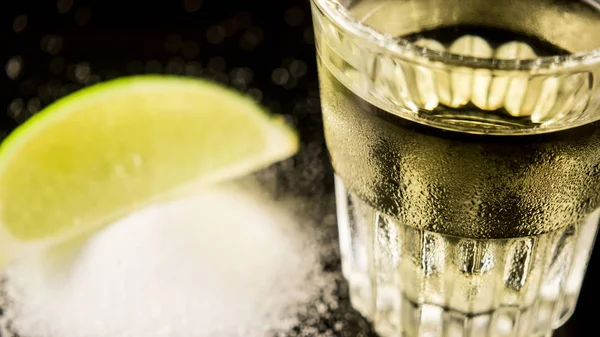 A shot of tequila on the table next to salt and lime — Stock Photo, Image