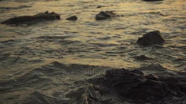 éclaboussure de petites vagues sur les rochers au coucher du soleil au ralenti 