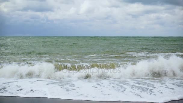 Au ralenti, une grosse vague bat contre une plage de galets 