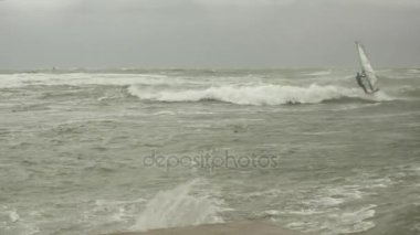 Gri gökyüzü altında fırtınalı denizde üç rüzgar sörfçüleri