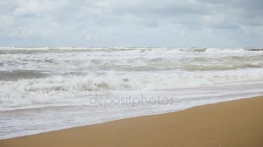 Fırtına dalgaları parlak gökyüzü altında kumlu bir plaj üzerinde