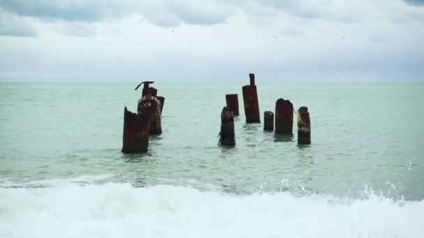 A kavicsos strandtól, a vízben a régi mólón roll a hullámok — Stock videók