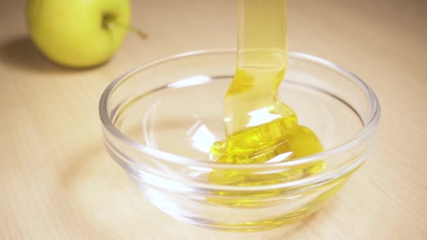La miel en cámara lenta fluye en un tazón sobre una mesa con una manzana — Vídeos de Stock