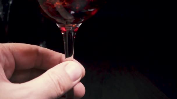 Los dedos masculinos sostienen el vidrio por la pierna. El vino está cayendo. — Vídeo de stock