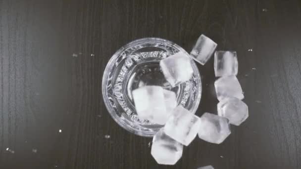 O gelo cai de cima em um copo e em uma mesa — Vídeo de Stock
