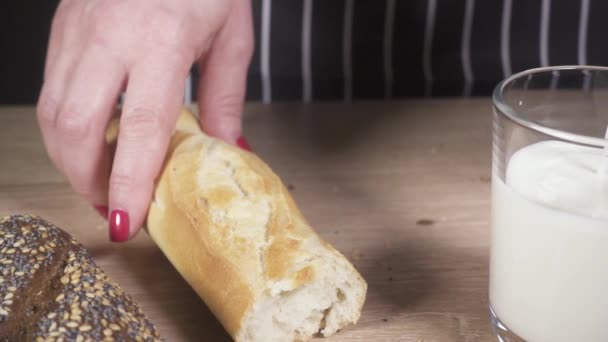 Vrouw houdt een stokbrood en giet de melk in een glas — Stockvideo