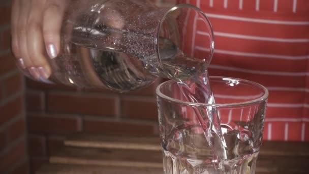 Cámara lenta una mujer en un delantal vierte agua en un vaso — Vídeos de Stock