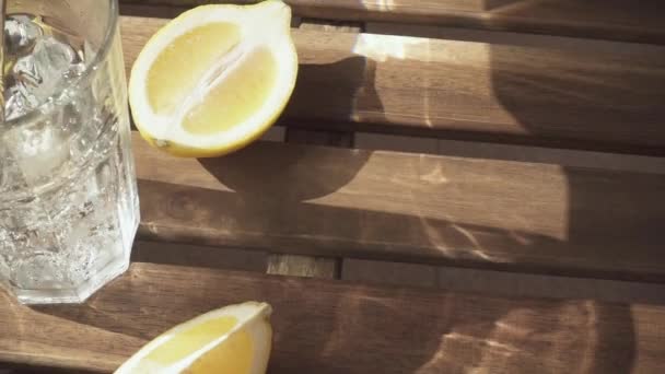 Rebanadas de limón en la mesa y el agua se vierte en un vaso de cámara lenta — Vídeos de Stock