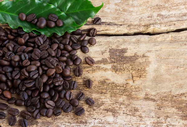 Grãos de café e folha verde no fundo de madeira — Fotografia de Stock