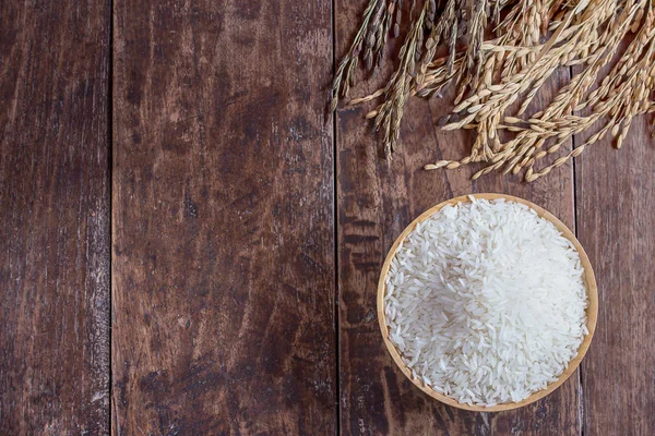 Jasmine rice in bowl and paddy rice on old wooden table — Stock Photo, Image