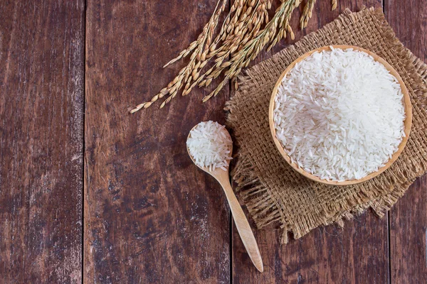 Jasmine rice in bowl and paddy rice on old wooden table — Stock Photo, Image