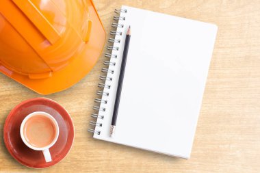 Safety helmet and cup of coffee with notebook on wooden table clipart