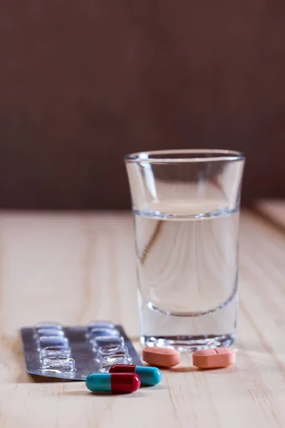 Pigułki i tabletki z szkło woda na drewnianym stole — Zdjęcie stockowe
