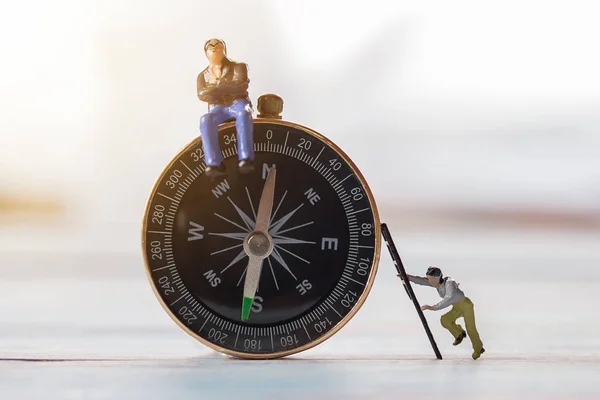 Miniature people- Figures businessman, is sitting on a compass a — Stock Photo, Image