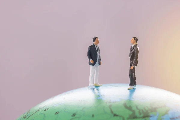 Two businessman figure standing on mini globe ball model.