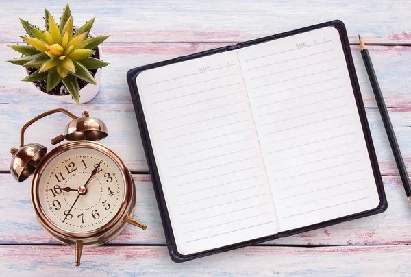 Reloj despertador retro, bloc de notas, lápiz y flor en una mesa de madera —  Fotos de Stock