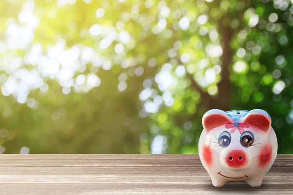 Sparschwein auf Holztisch mit unscharfem grünen Bokeh-Hintergrund und — Stockfoto