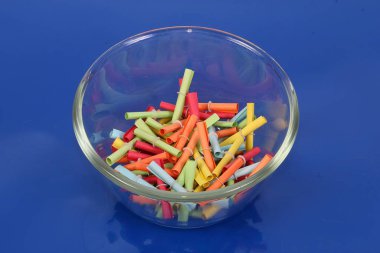 Mavi arka planda küçük bir cam kasede gevşek duran renkli tombala.