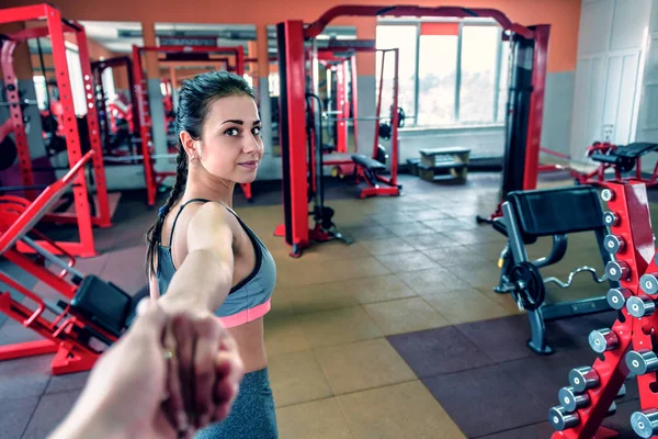 Beni takip edin. Spor elbiseli genç bir kadın spor salonunda erkek arkadaşının elini tutuyor.