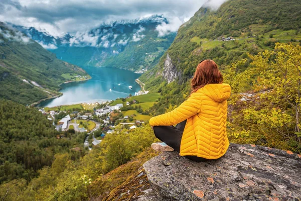 A woman in a yellow down jacket sits over a Norwegian fjord — Stockfoto