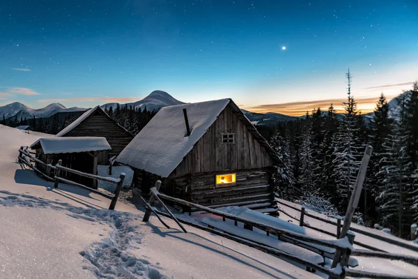 Luz en las cabañas ventana en las montañas de invierno — Foto de Stock