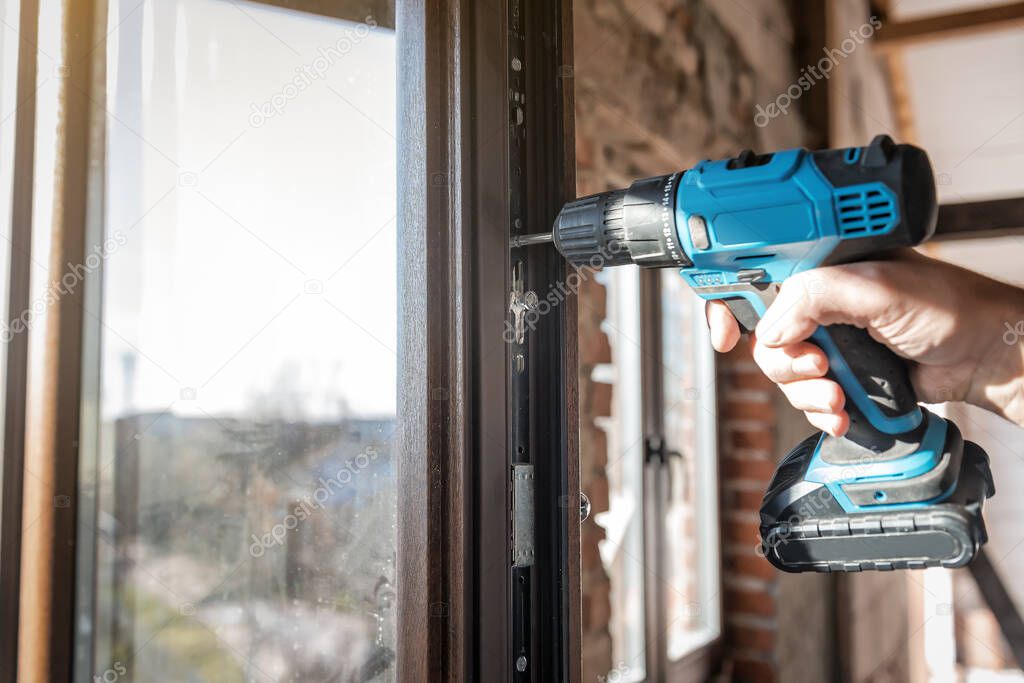 worker with professional electric screwdriver adjusts the window