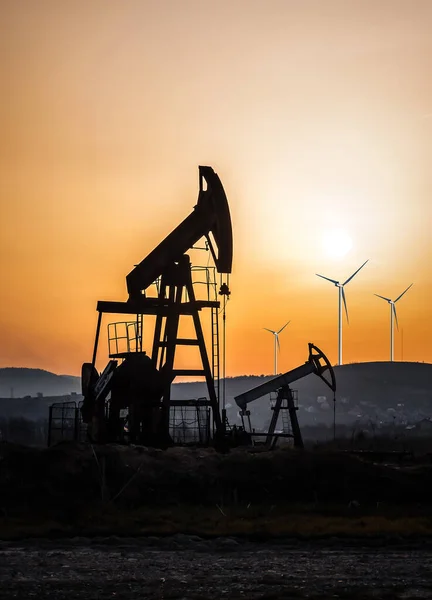 日没時の石油ポンプと風車のシルエット — ストック写真