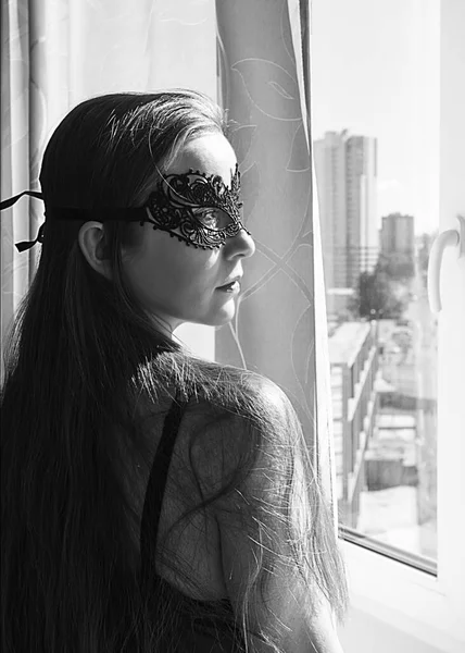 Sexy woman in black lace mask stands near the window. — Stock Photo, Image