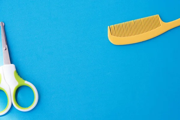 Çocuklar için plastik sarı tarak ve yeşil güvenlik makası, mavi arkaplan üst görünümü