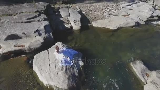Una ragazza si siede su una roccia in mezzo al fiume — Video Stock