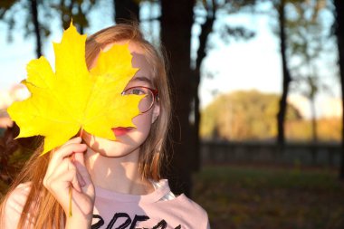 Yüzünün yarısını kaplayan sarı akçaağaç yaprağı olan genç kız.