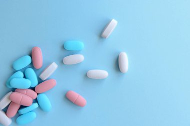 Çeşitli ilaç hapları, haplar ve kapsüller mavi arka planda.