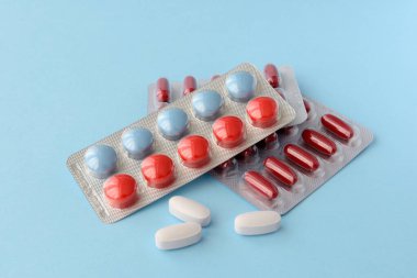 Çeşitli ilaç hapları, haplar ve kapsüller mavi arka planda.