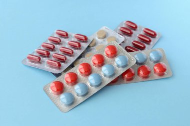 Çeşitli ilaç hapları, haplar ve kapsüller mavi arka planda.