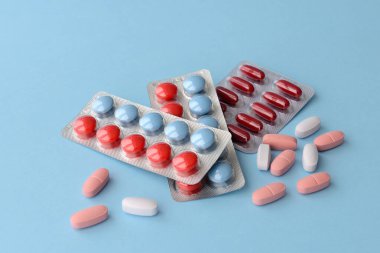 Çeşitli ilaç hapları, haplar ve kapsüller mavi arka planda.
